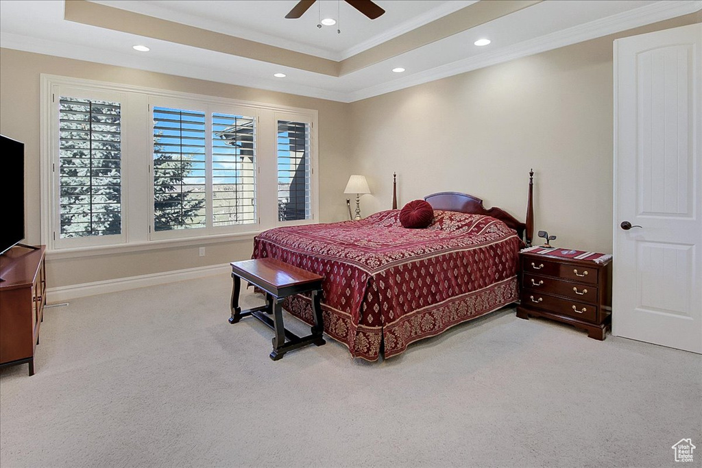 Bedroom with ornamental molding, a tray ceiling, light carpet, and ceiling fan
