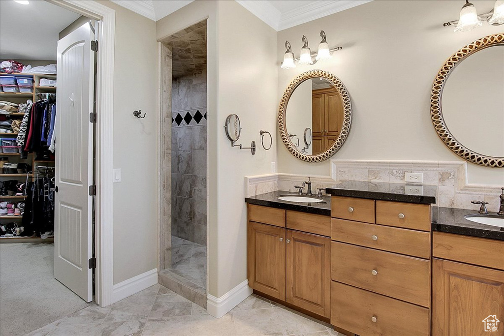 Bathroom featuring tiled shower, ornamental molding, double sink vanity, and tile floors
