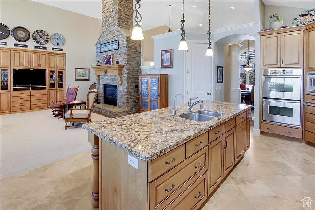 Kitchen with a fireplace, a kitchen island with sink, sink, hanging light fixtures, and appliances with stainless steel finishes