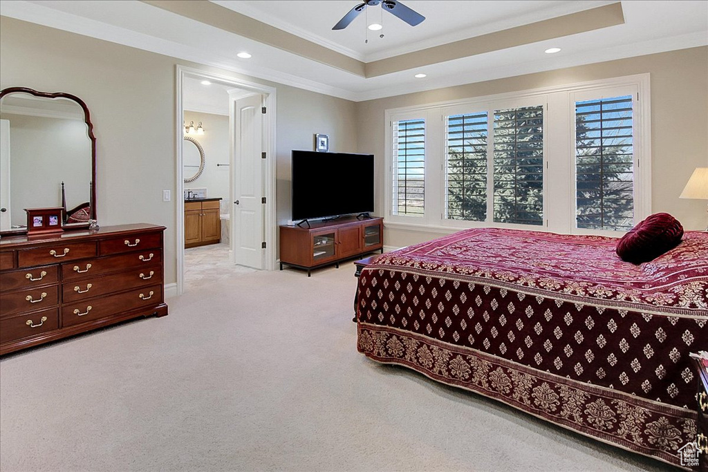 Bedroom with a raised ceiling, light carpet, connected bathroom, and ceiling fan
