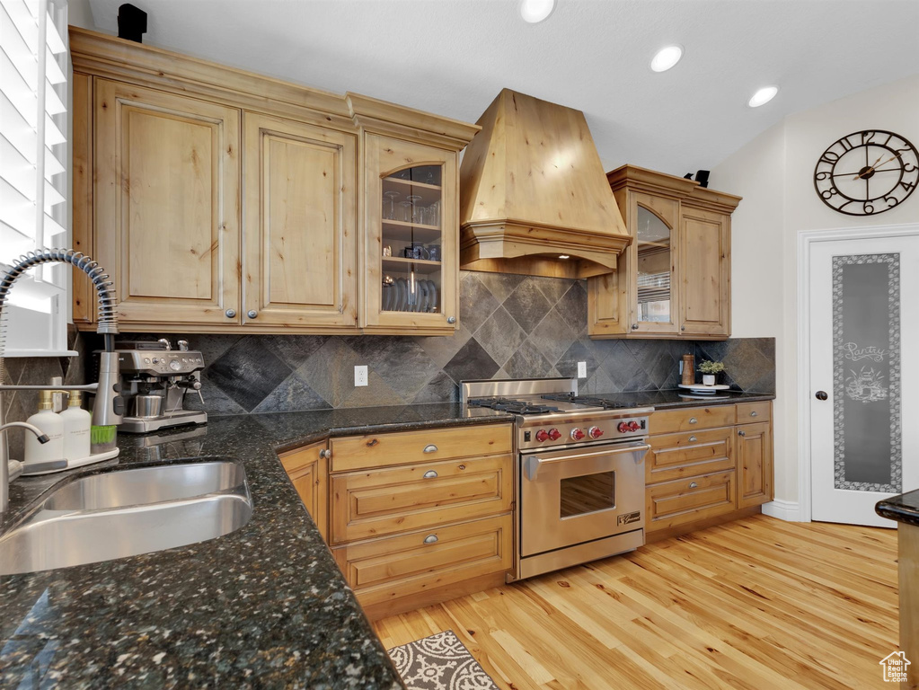 Kitchen with backsplash, custom exhaust hood, designer range, sink, and light hardwood / wood-style flooring