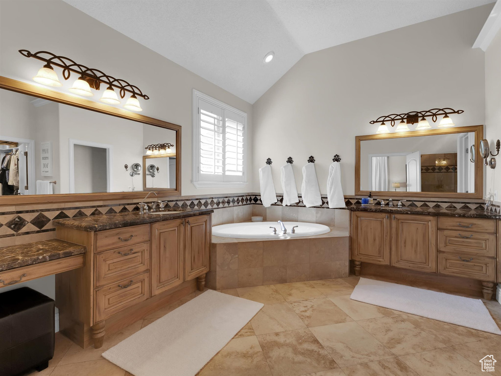 Bathroom with vanity, tile flooring, tiled bath, and lofted ceiling