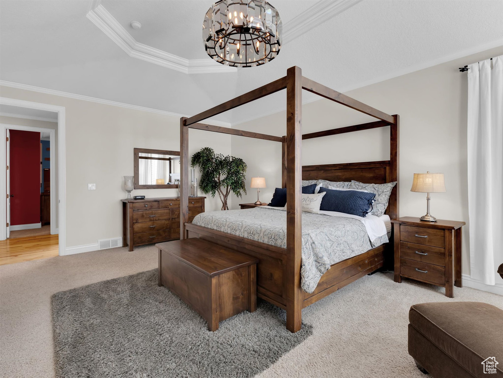 Bedroom featuring a raised ceiling, ornamental molding, light carpet, and a chandelier