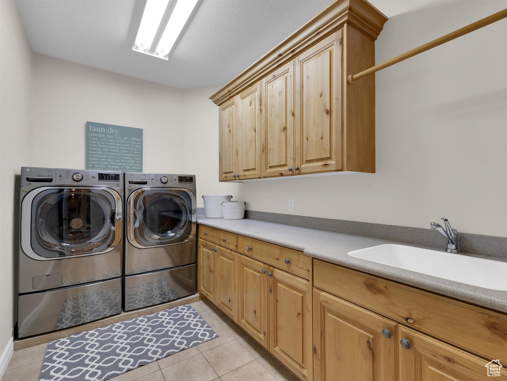 Washroom with light tile floors, washer and dryer, sink, and cabinets