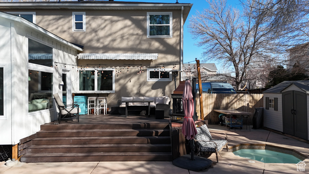Back of property featuring an outdoor hot tub, a patio area, a shed, and a wooden deck