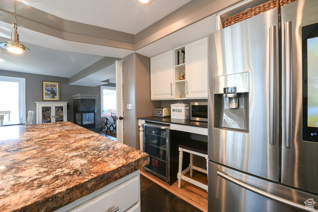 Kitchen featuring beverage cooler, stainless steel appliances, dark tile flooring, white cabinets, and pendant lighting
