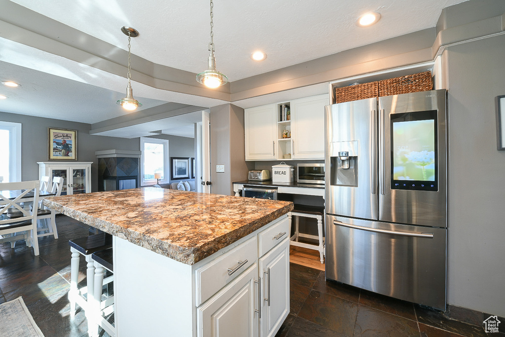 Kitchen featuring white cabinets, stainless steel fridge with ice dispenser, a center island, and hanging light fixtures