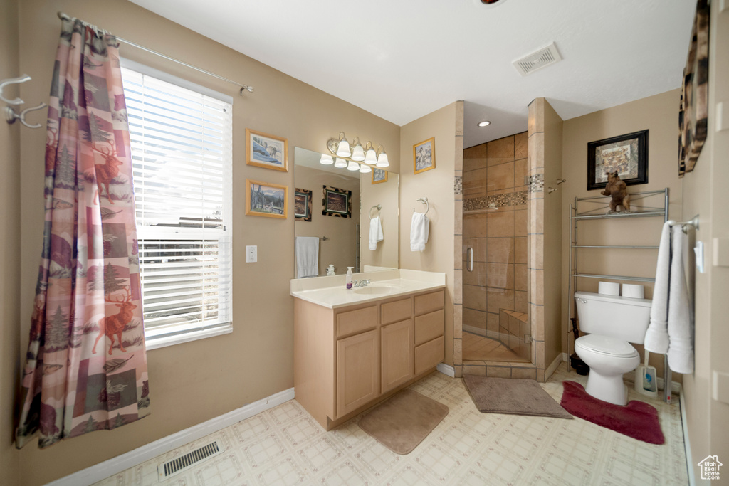 Bathroom with toilet, a tile shower, a healthy amount of sunlight, and oversized vanity