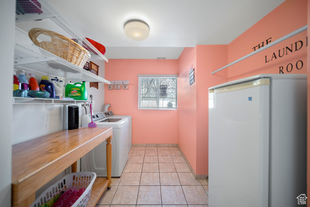 Washroom with light tile flooring and washing machine and clothes dryer