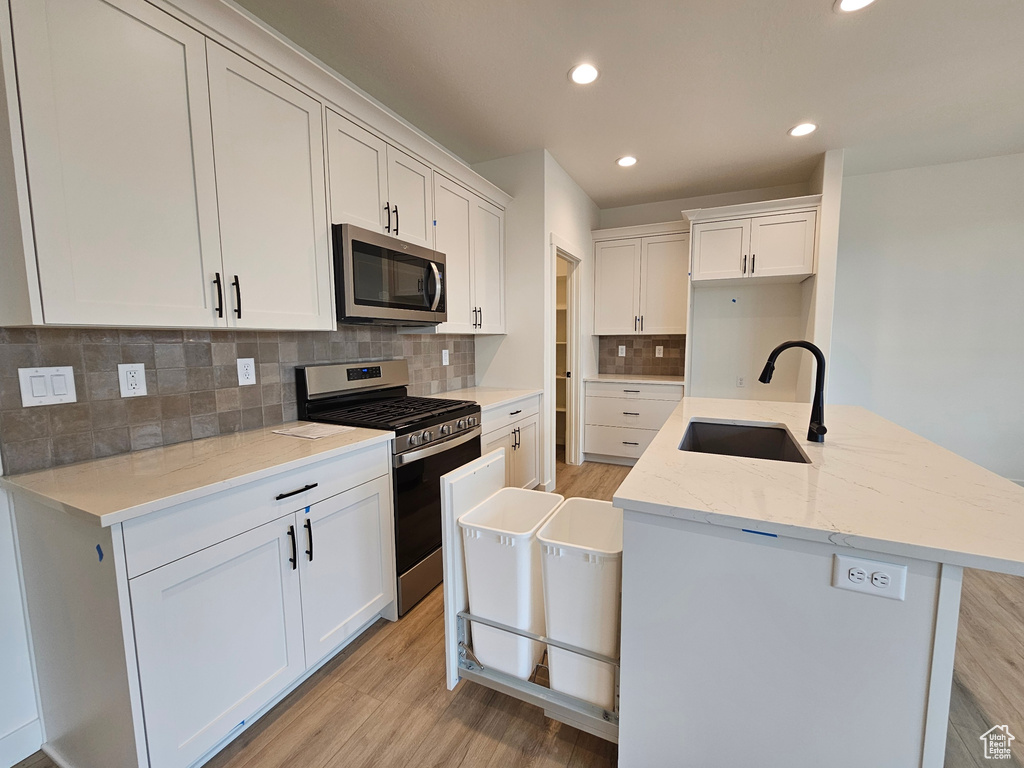 Kitchen featuring backsplash, appliances with stainless steel finishes, white cabinets, and light wood-type flooring