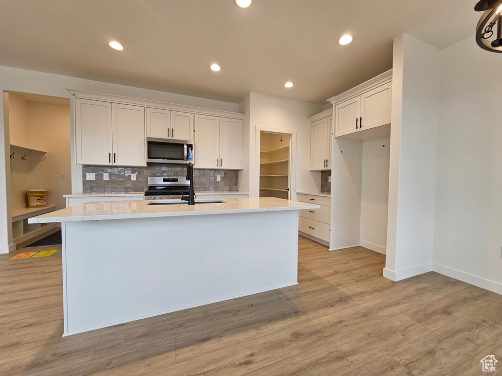 Kitchen with white cabinets, light hardwood / wood-style floors, a center island with sink, and range