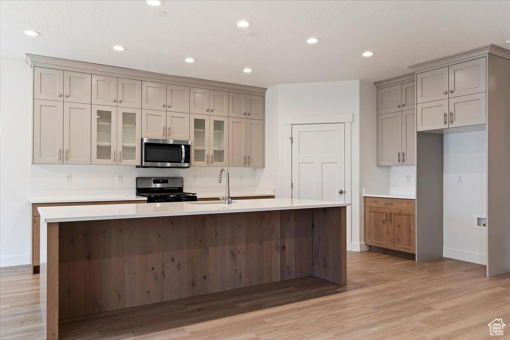 Kitchen with range with gas cooktop, an island with sink, light hardwood / wood-style flooring, sink, and gray cabinets