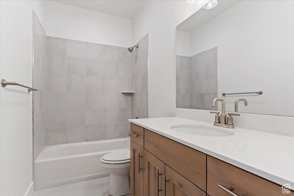 Full bathroom with tile flooring, large vanity, toilet, and tiled shower / bath