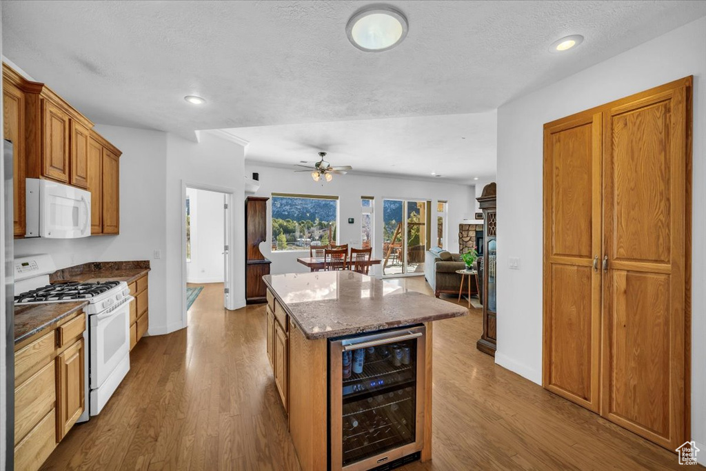 Kitchen with white appliances, ceiling fan, light hardwood / wood-style flooring, a stone fireplace, and beverage cooler