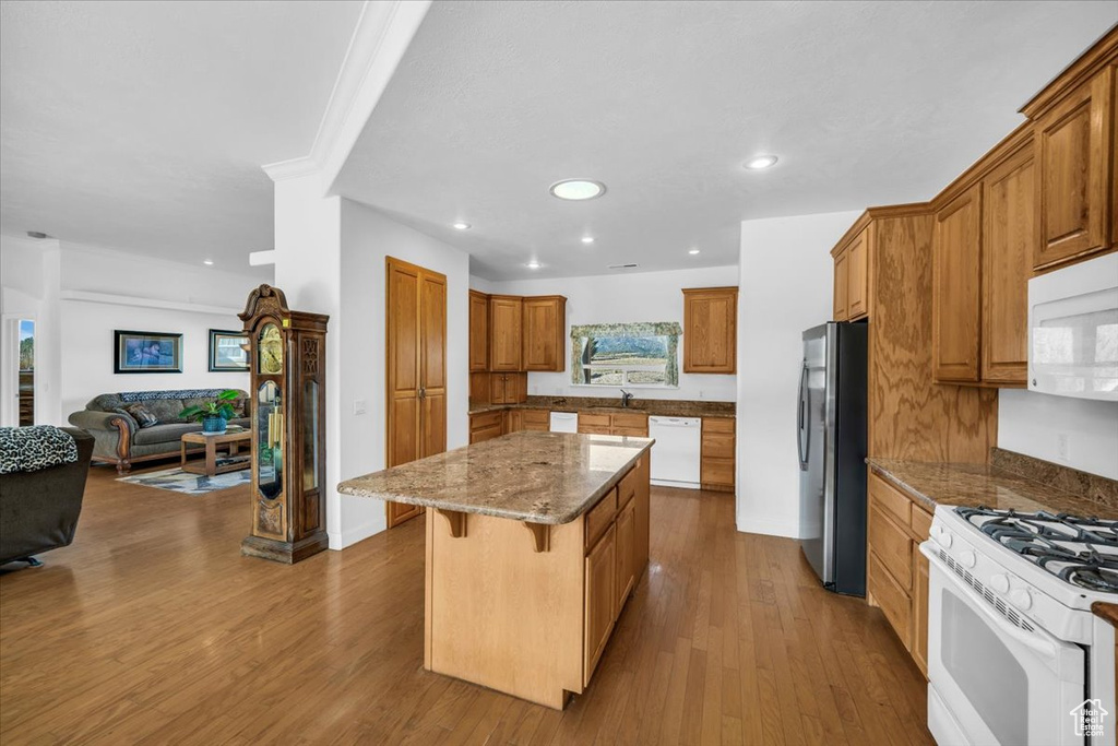 Kitchen featuring wood-type flooring, a kitchen island, white appliances, and a kitchen breakfast bar