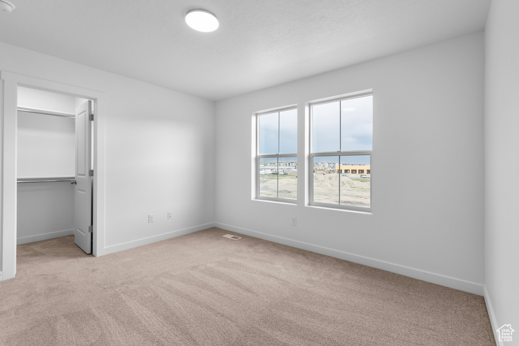 Unfurnished bedroom featuring a spacious closet, light carpet, a closet, and a water view