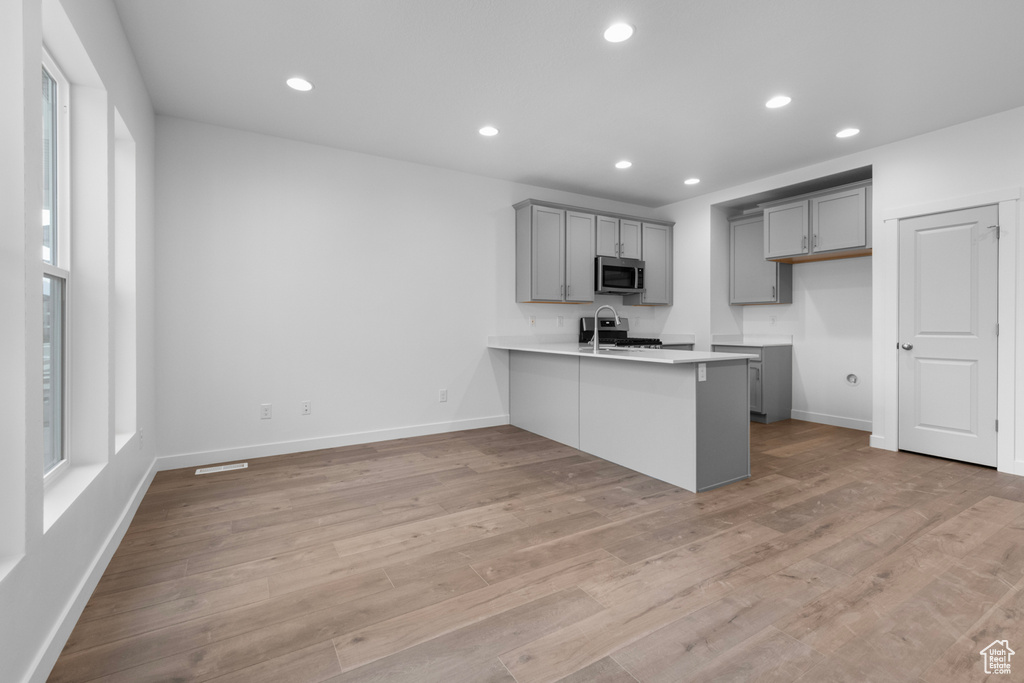 Kitchen with gray cabinets, light hardwood / wood-style flooring, kitchen peninsula, appliances with stainless steel finishes, and a kitchen bar