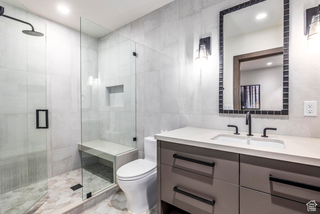 Bathroom with tile walls, tile flooring, a shower with shower door, vanity, and toilet