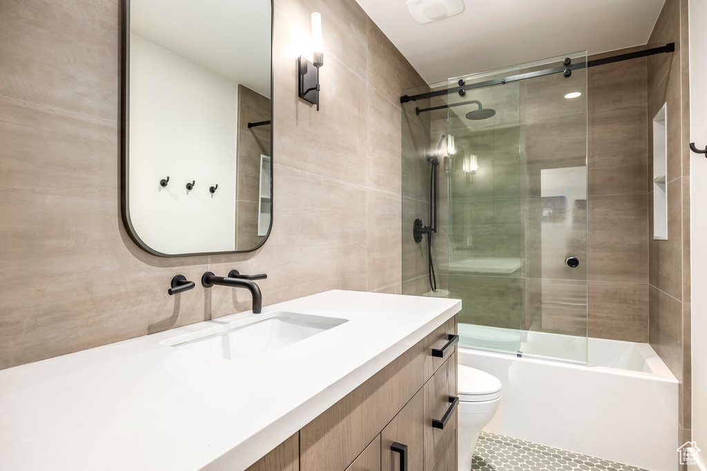 Full bathroom featuring vanity, tile walls, toilet, tile flooring, and bath / shower combo with glass door
