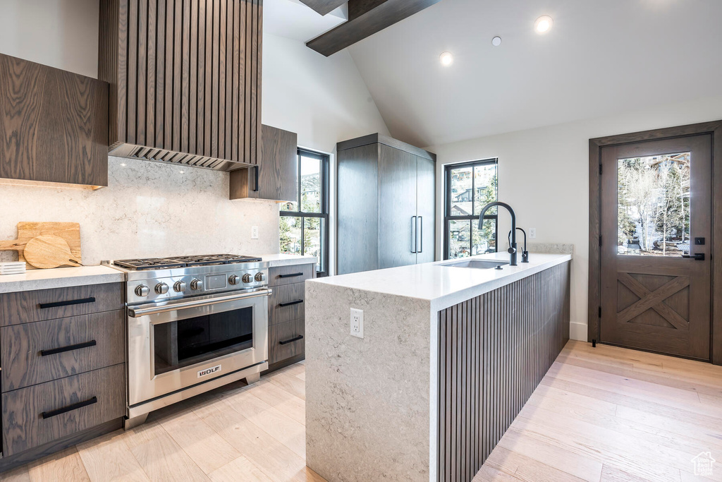 Kitchen featuring stainless steel range, sink, premium range hood, beamed ceiling, and light wood-type flooring