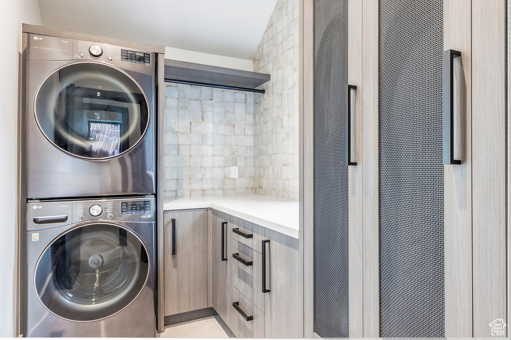 Washroom featuring stacked washer and clothes dryer, light tile flooring, and cabinets