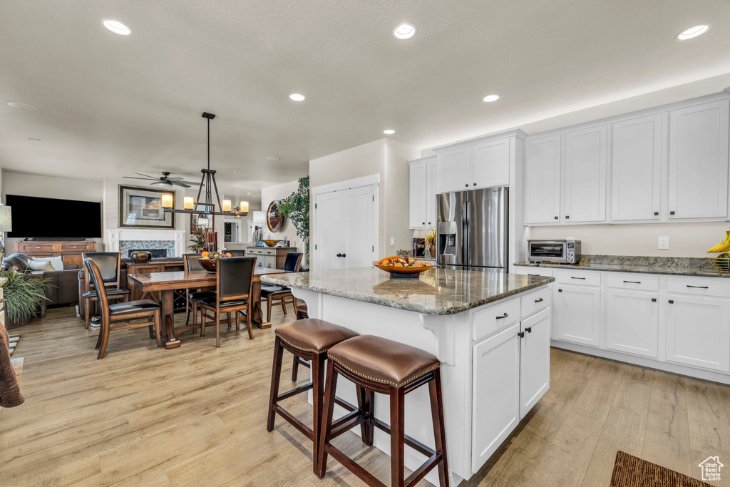Kitchen with stainless steel fridge with ice dispenser, dark stone countertops, hanging light fixtures, light hardwood / wood-style flooring, and a center island
