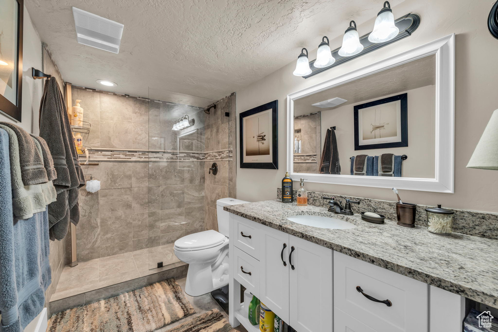 Bathroom with tiled shower, toilet, vanity, and a textured ceiling
