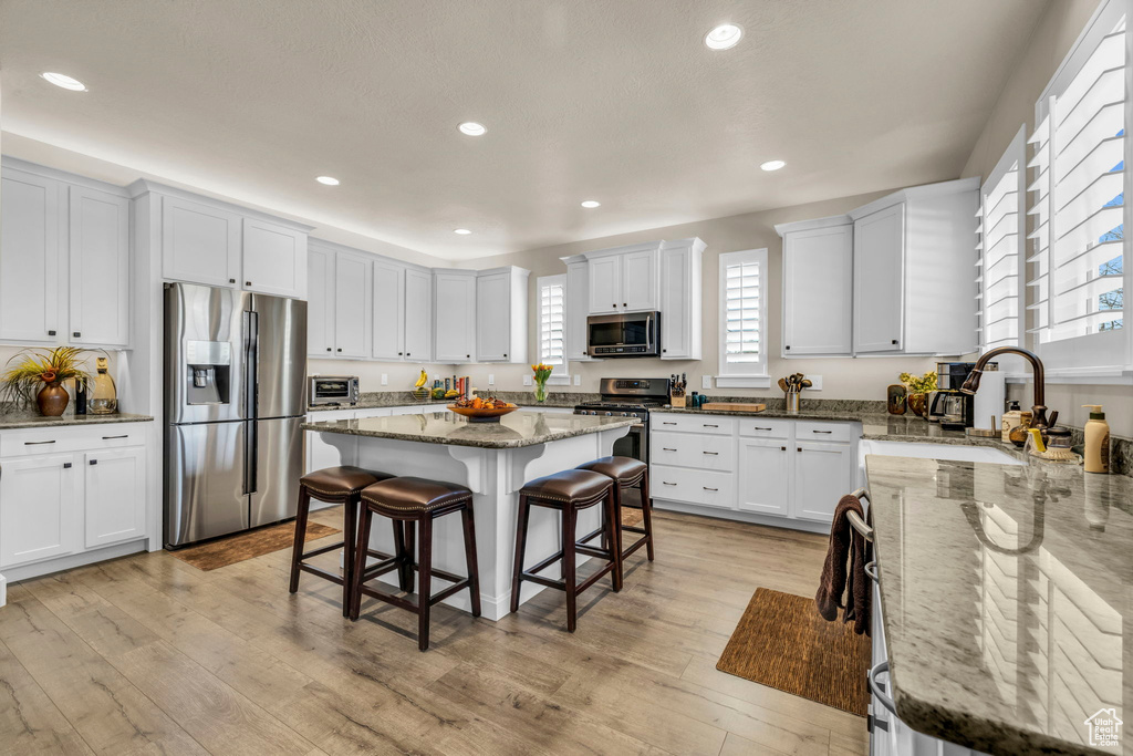 Kitchen featuring a kitchen island, light hardwood / wood-style flooring, stainless steel appliances, light stone counters, and a breakfast bar area