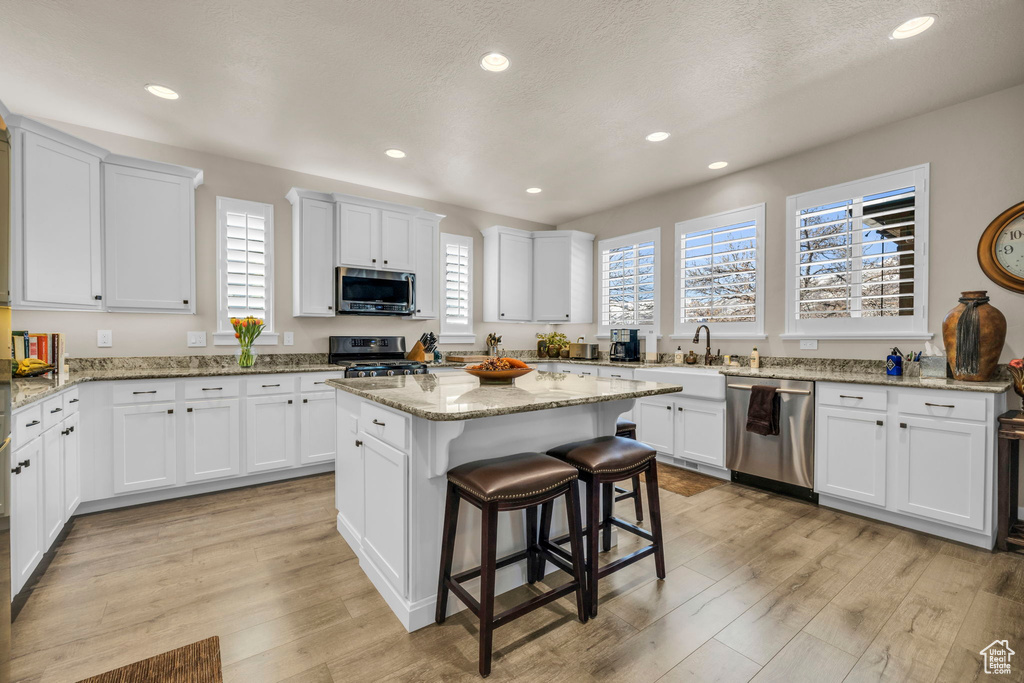 Kitchen featuring white cabinets, stainless steel appliances, light hardwood / wood-style floors, light stone counters, and a kitchen island