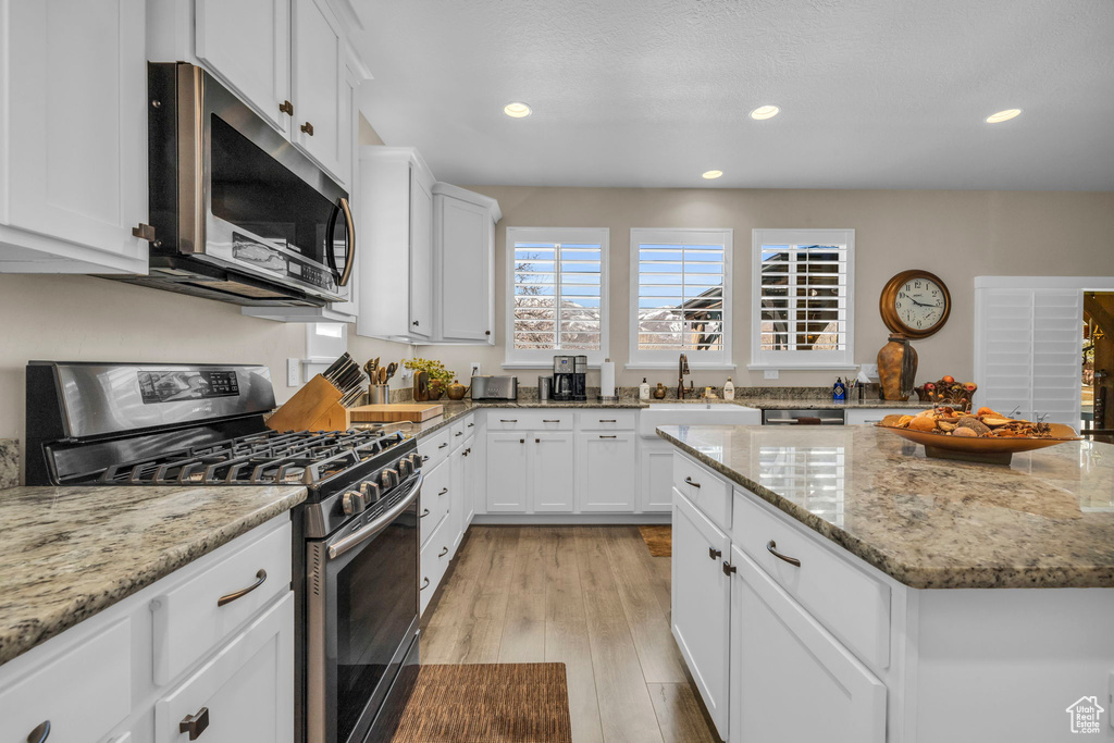 Kitchen featuring sink, white cabinets, light hardwood / wood-style floors, stainless steel appliances, and light stone counters