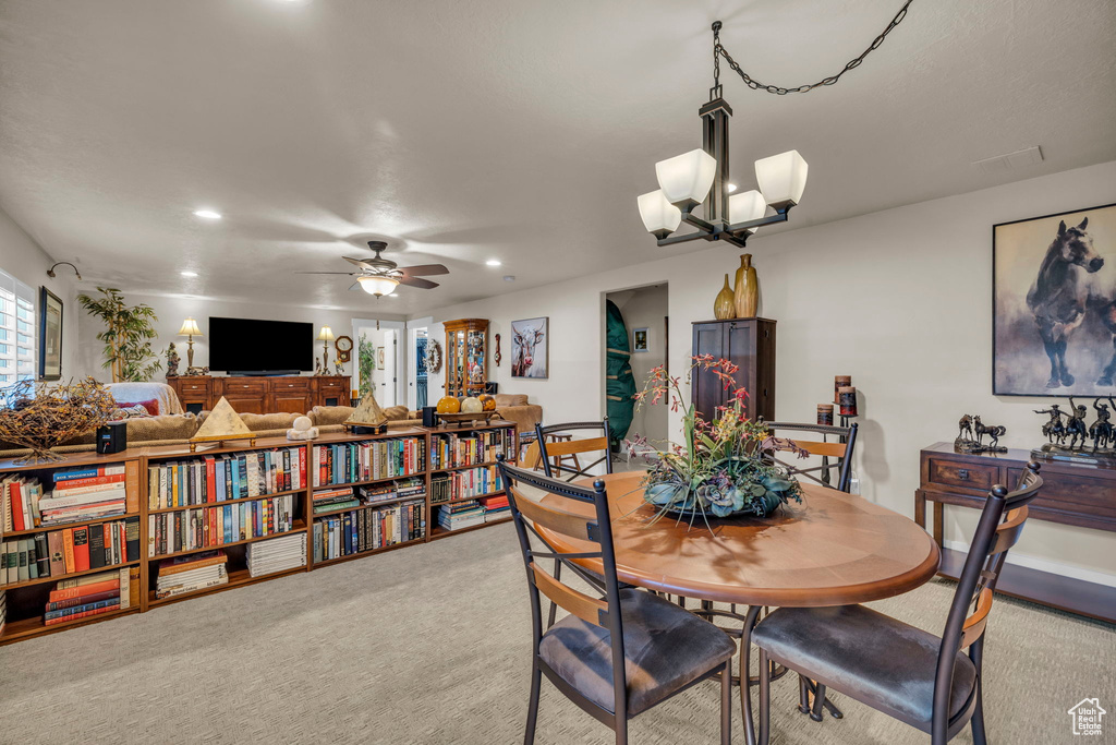 Carpeted dining area with ceiling fan with notable chandelier