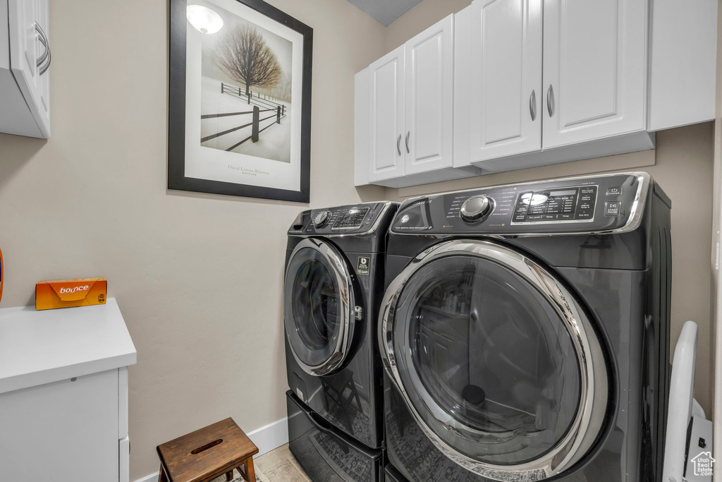 Clothes washing area featuring washing machine and dryer, cabinets, and light tile floors
