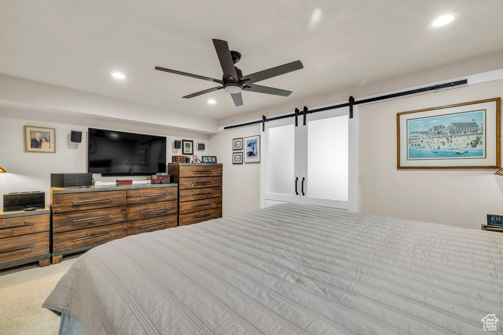 Bedroom featuring light carpet, ceiling fan, and a barn door