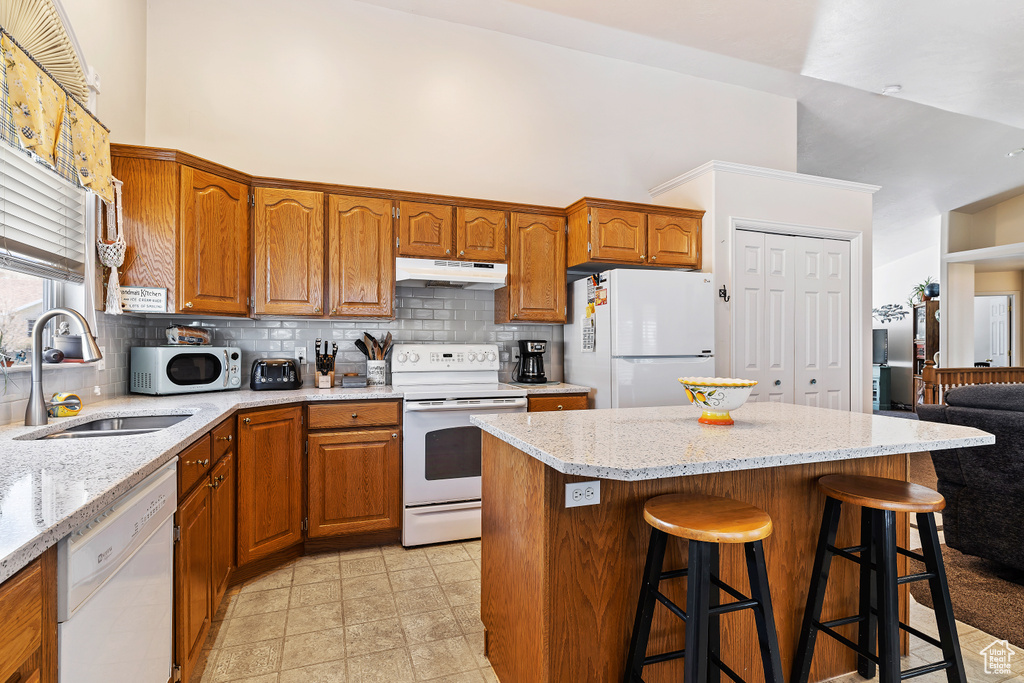 Kitchen with backsplash, light tile floors, white appliances, sink, and a kitchen bar