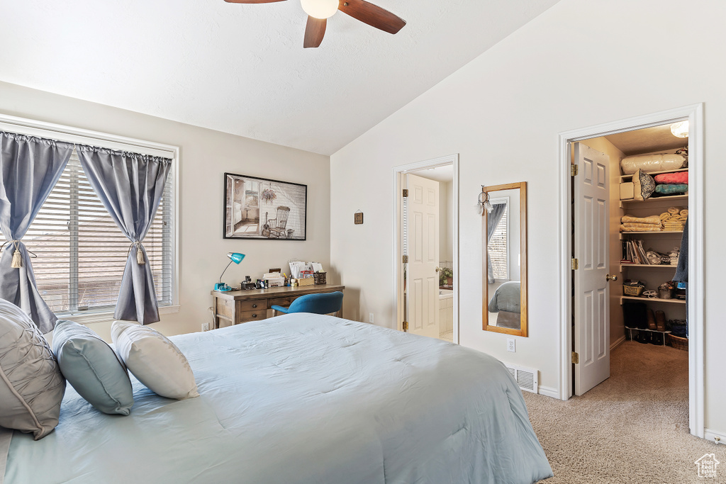 Carpeted bedroom featuring vaulted ceiling, a walk in closet, ensuite bath, and ceiling fan