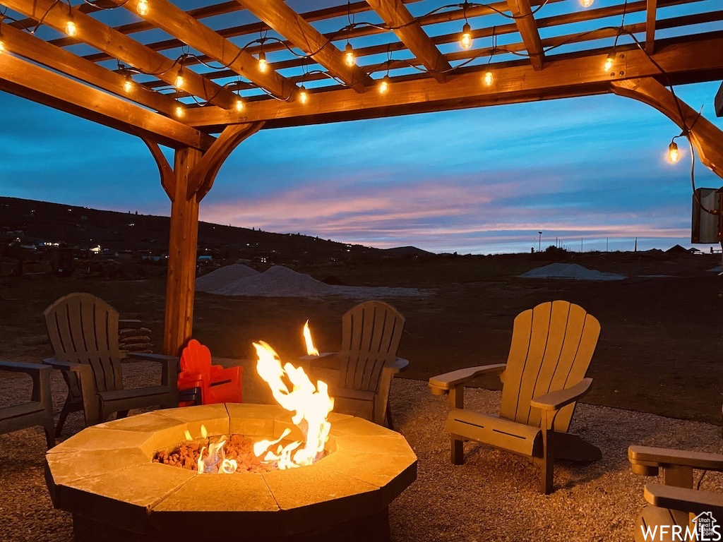 Patio terrace at dusk featuring a pergola and a fire pit