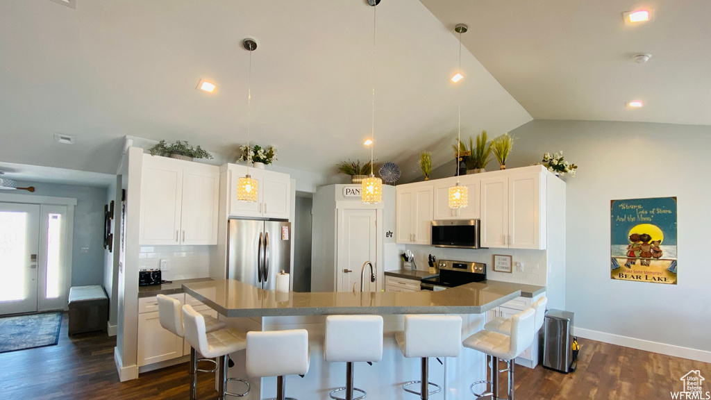 Kitchen featuring dark hardwood / wood-style floors, white cabinets, decorative light fixtures, an island with sink, and appliances with stainless steel finishes