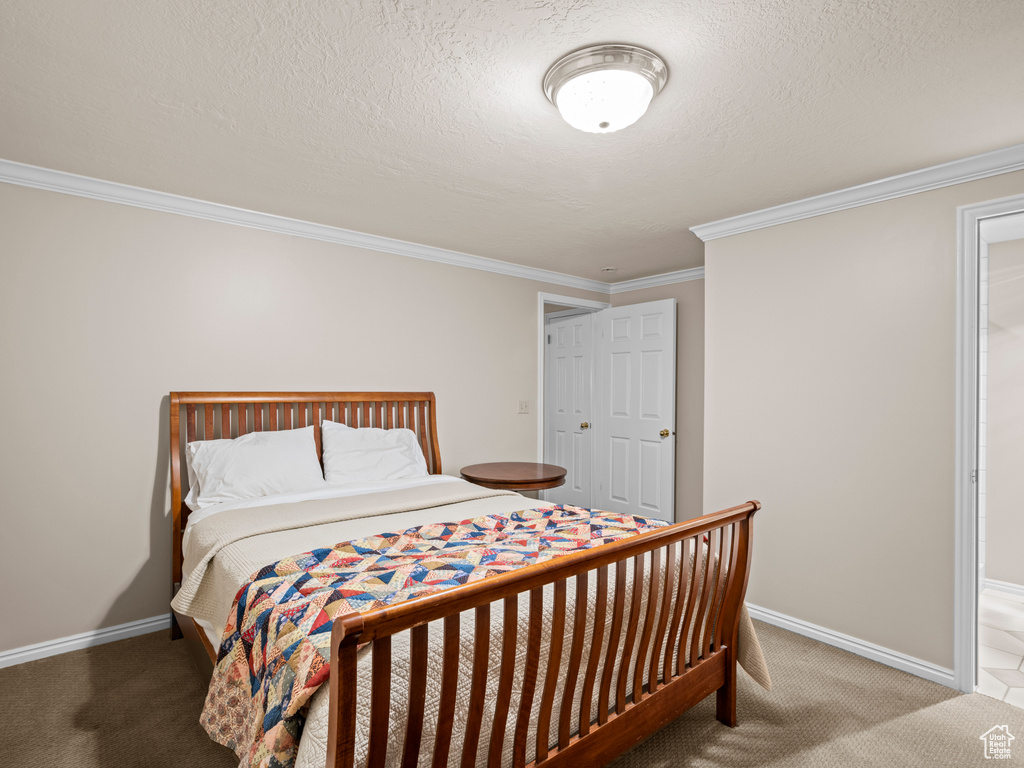 Bedroom with light colored carpet, crown molding, and a textured ceiling