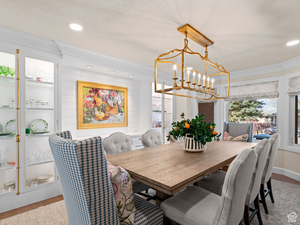 Dining space with a chandelier, a textured ceiling, light hardwood / wood-style floors, and crown molding
