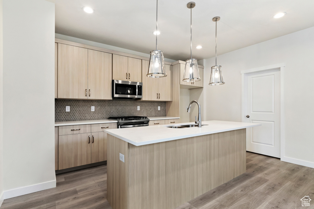 Kitchen featuring sink, tasteful backsplash, hanging light fixtures, appliances with stainless steel finishes, and light hardwood / wood-style flooring