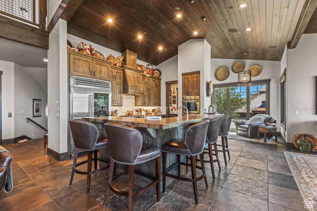 Kitchen with stainless steel appliances, a kitchen bar, wood ceiling, and high vaulted ceiling