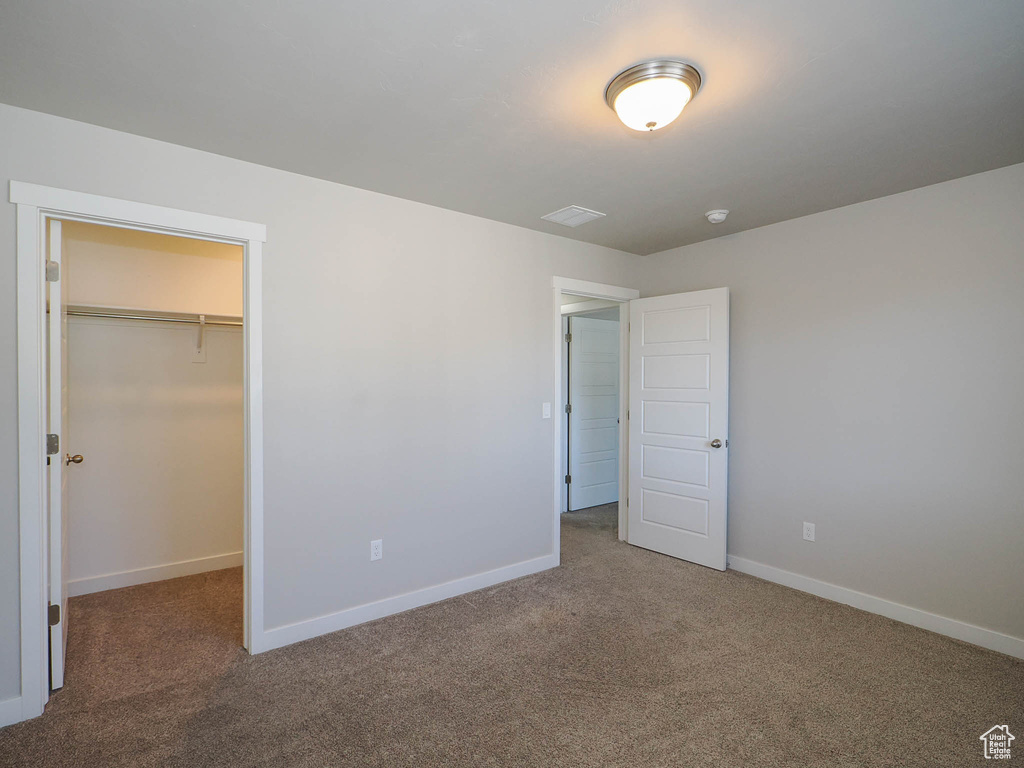 Unfurnished bedroom with dark carpet, a closet, and a walk in closet
