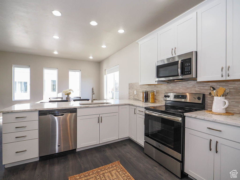Kitchen with appliances with stainless steel finishes, white cabinets, sink, and dark wood-type flooring