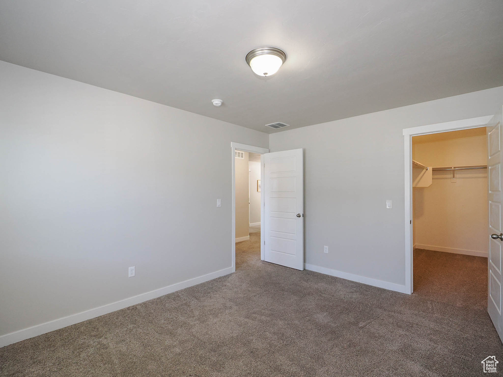 Unfurnished bedroom with a walk in closet, a closet, and dark colored carpet