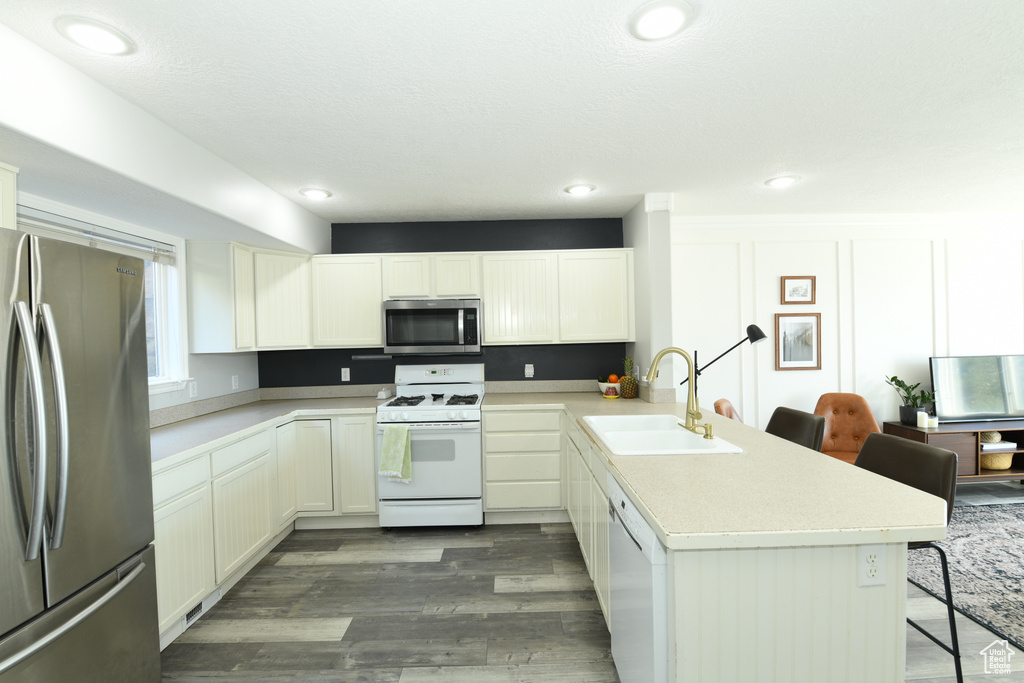 Kitchen with kitchen peninsula, stainless steel appliances, dark wood-type flooring, sink, and a kitchen bar