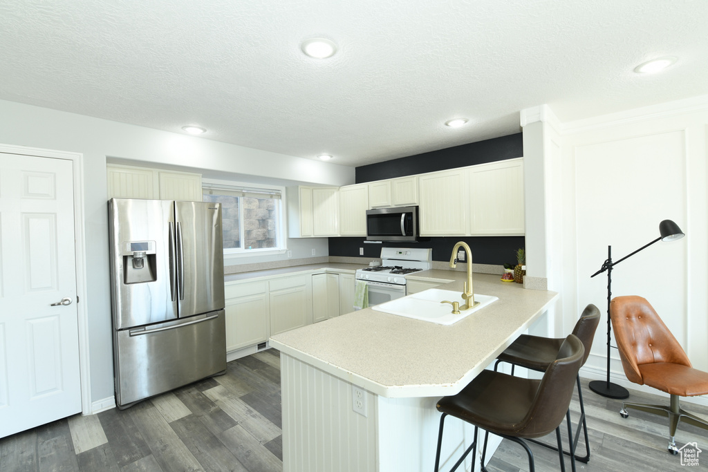 Kitchen featuring kitchen peninsula, stainless steel appliances, sink, dark hardwood / wood-style flooring, and a kitchen bar
