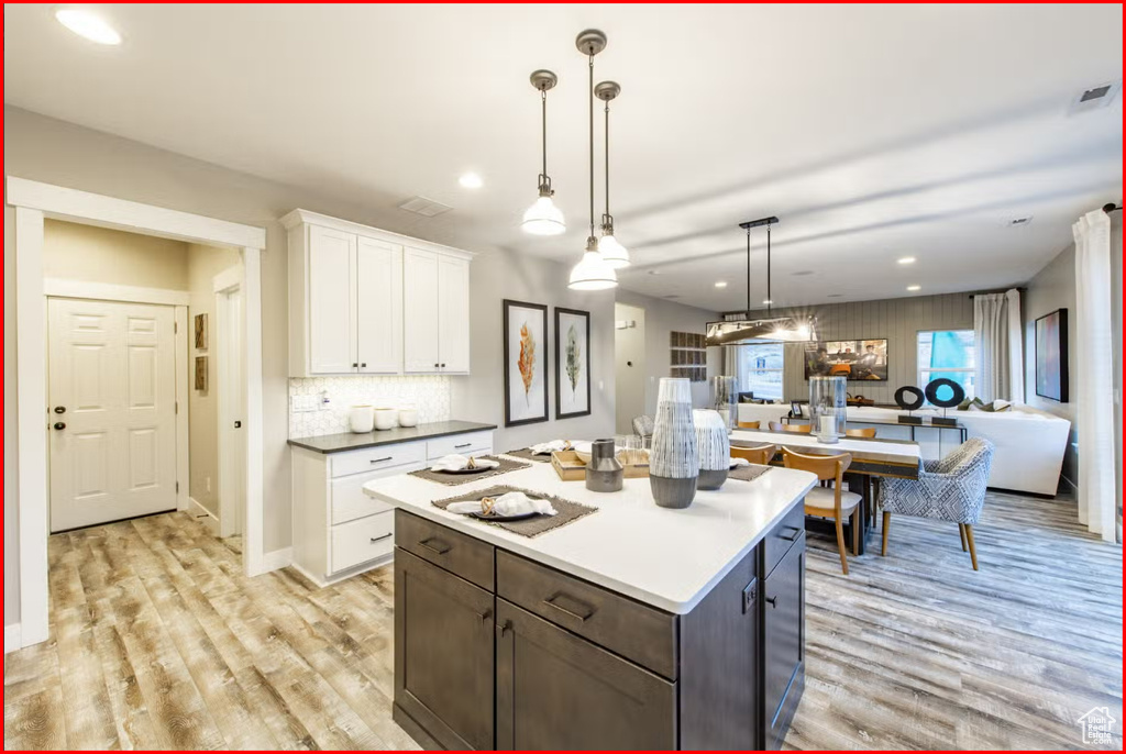 Kitchen with a kitchen island, light hardwood / wood-style floors, white cabinets, and decorative light fixtures