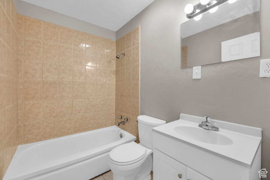 Full bathroom featuring a textured ceiling, toilet, vanity with extensive cabinet space, and tiled shower / bath