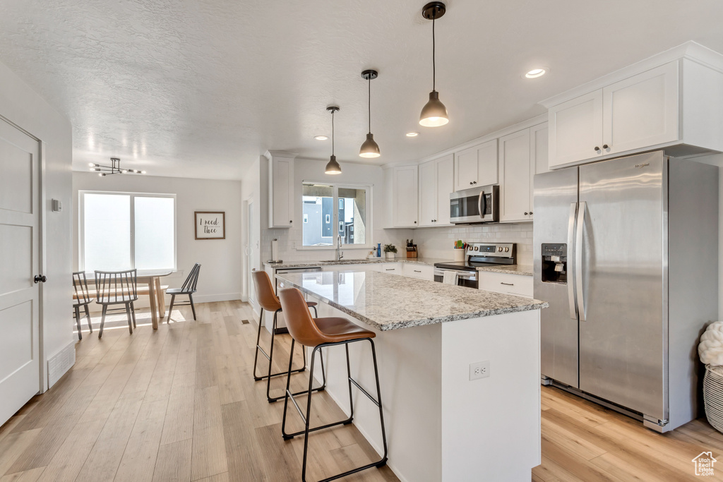 Kitchen featuring white cabinetry, hanging light fixtures, appliances with stainless steel finishes, light hardwood / wood-style flooring, and light stone countertops