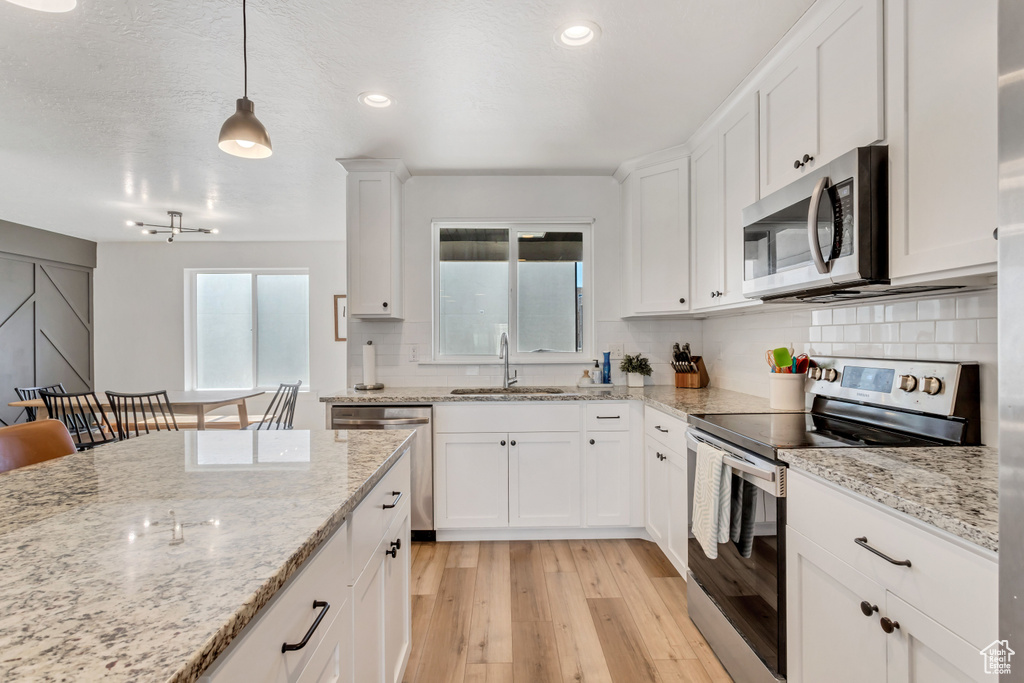 Kitchen featuring sink, pendant lighting, light hardwood / wood-style floors, backsplash, and stainless steel appliances